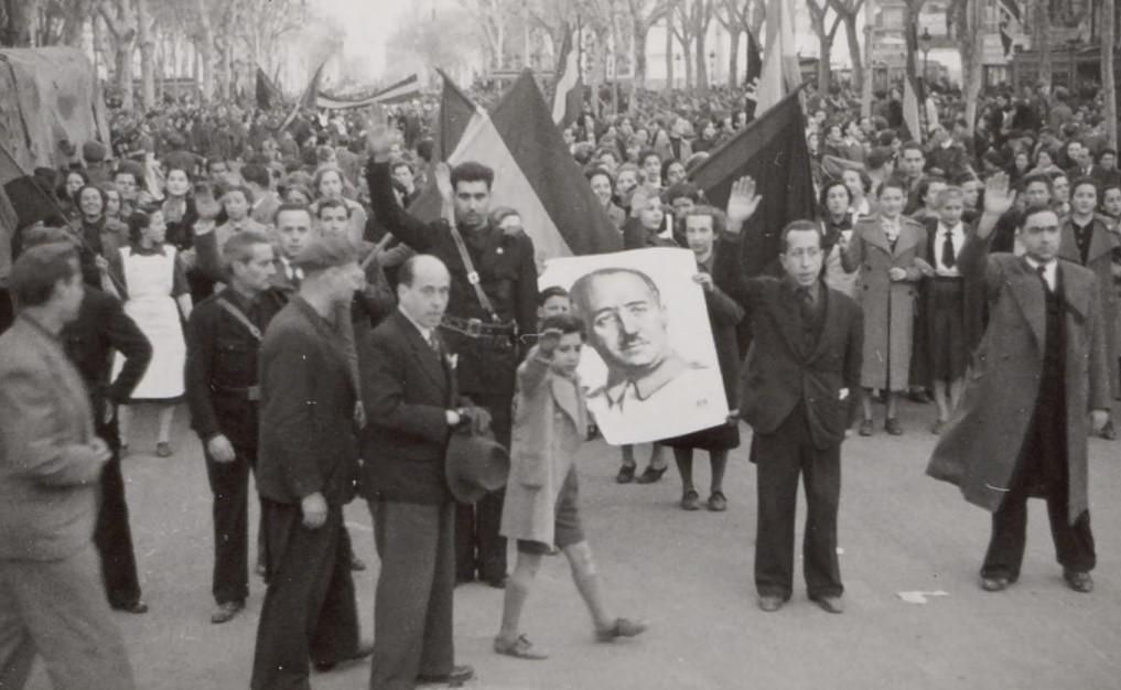 Varias personas sujetan una imagen de Franco mientras hacen el saludo fascista.