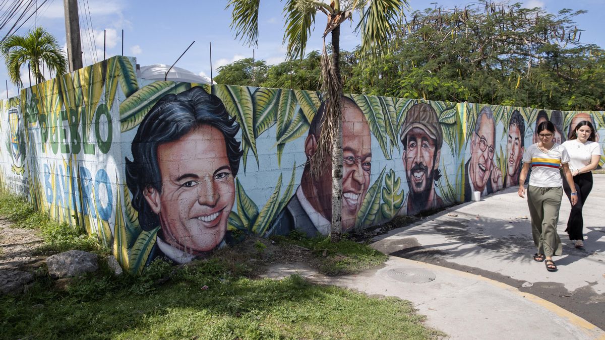 Vecinos caminan frente a un mural con los rostros de los artistas Julio Iglesias, Johnny Ventura y Juan Luis Guerra en Bávaro (República Dominicana).