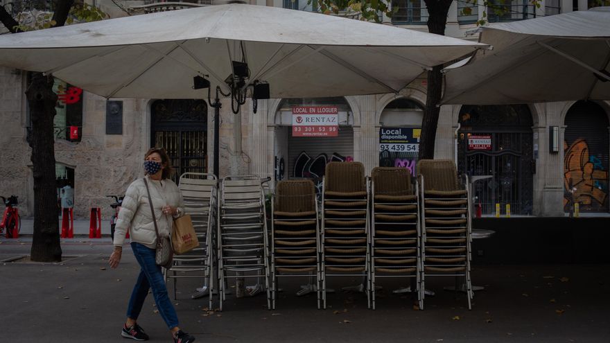 Una mujer pasa junto a la terraza recogida de un bar cerrado durante el cuarto día de la entrada en vigor de las nuevas restricciones en Cataluña.