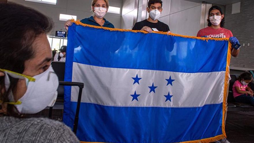 Un grupo de hondureños varados en Estados Unidos por el coronavirus sostienen la bandera nacional ante de subir a un avión este sábado en el Aeropuerto Internacional de Fort Lauderdale, a 40 kilómetros al norte de Miami, Florida (EEUU). Un vuelo especial de la compañía Spirit se llevó este sábado de regreso a su país a 150 hondureños a los que el cierre de fronteras por el COVID-19 sorprendió estando de visita en EE.UU. y quedaron varados, una situación en la que todavía están muchos otros que esperan una nueva oportunidad para viajar.