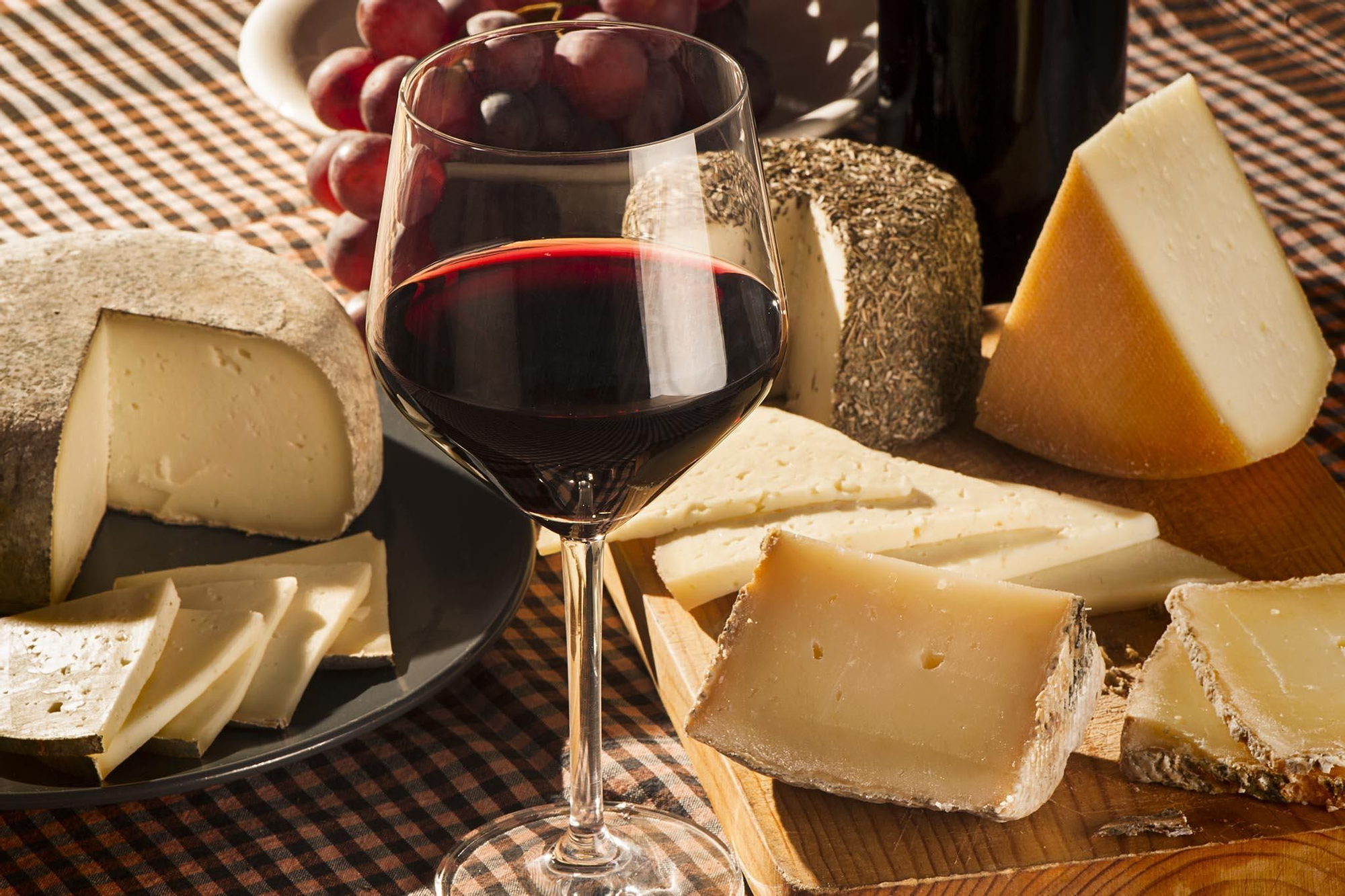 Bodegó amb una copa de vi negre acompanyada de raïm i formatges artesanals catalans