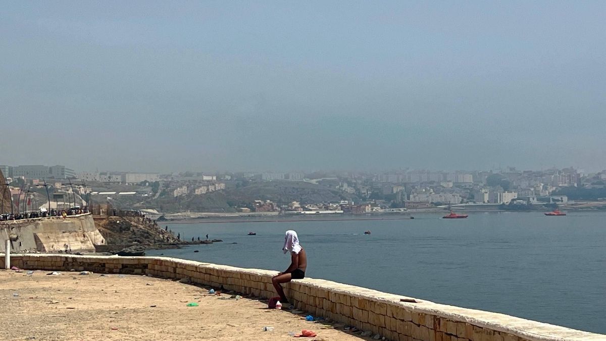 Un joven descansa en Castillejos, al otro lado de la frontera con Ceuta. De fondo se puede ver la nueva "barrera" flotante colocada por el Gobierno en el mar.