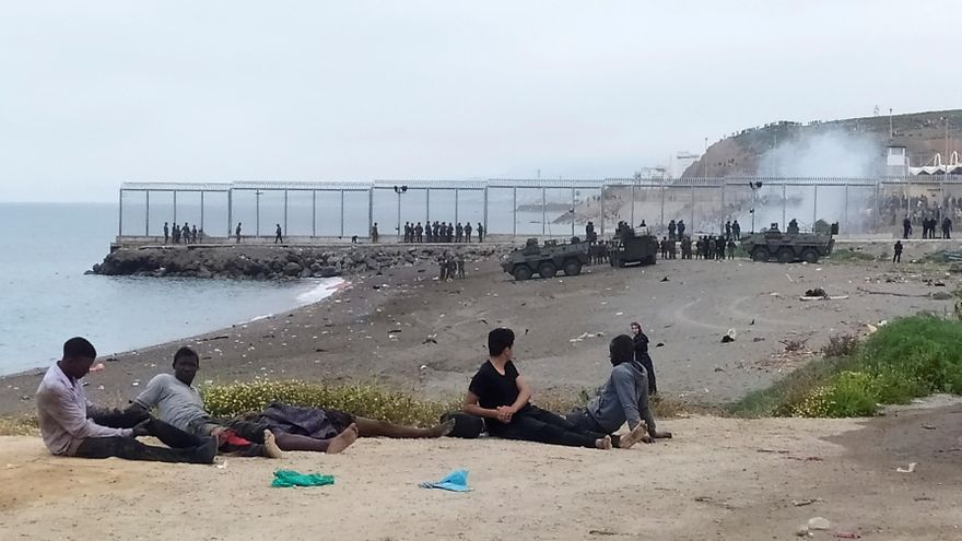 Un grupo de inmigrantes marroquí observa el despliegue del Ejército de Tierra en uno de los espigones fronterizos de Ceuta, donde ayer se batió la cifra récord de llegada de inmigrantes a España en un solo día por vía marítima, contabilizando los 5000 marroquíes que según la delegación del gobierno en Ceuta han llegado a la ciudad autónoma. EFE/Reduan