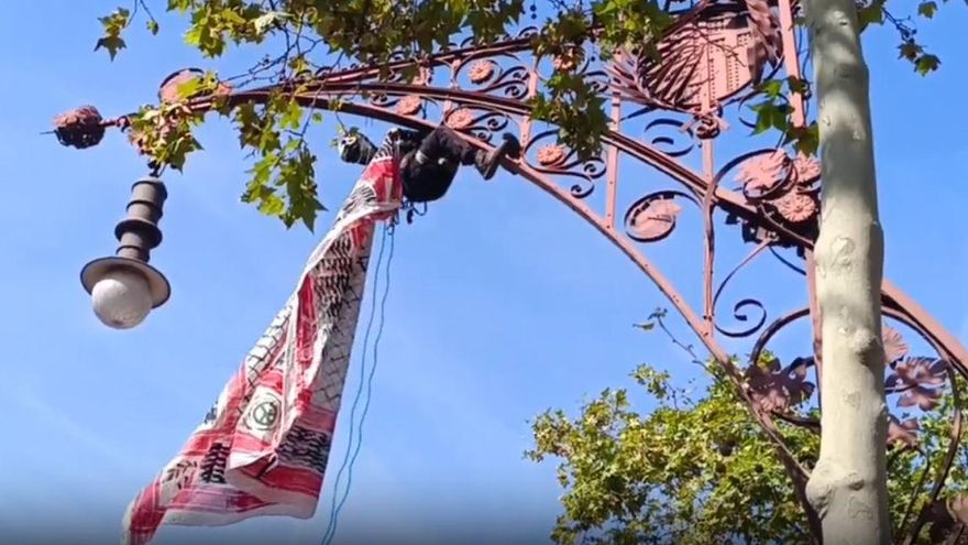 Un escalador cuelga una kufiya palestina de una farola durante la manifestación de Barcelona.