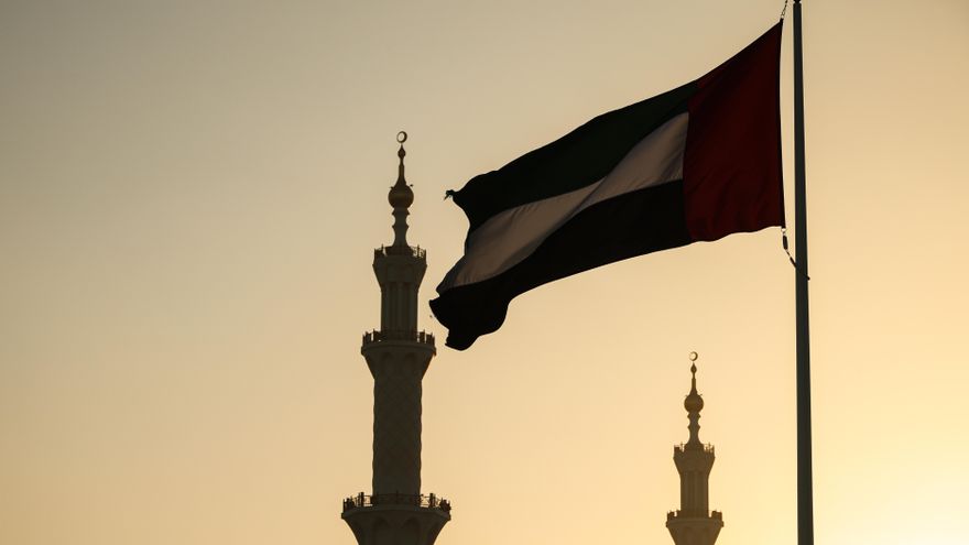 Una bandera de Emiratos Árabes Unidos y minaretes de mezquitas en Abu Dabi.