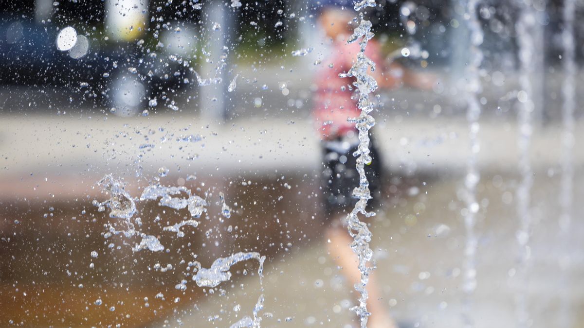 Una persona se refresca del calor en una fuente pública