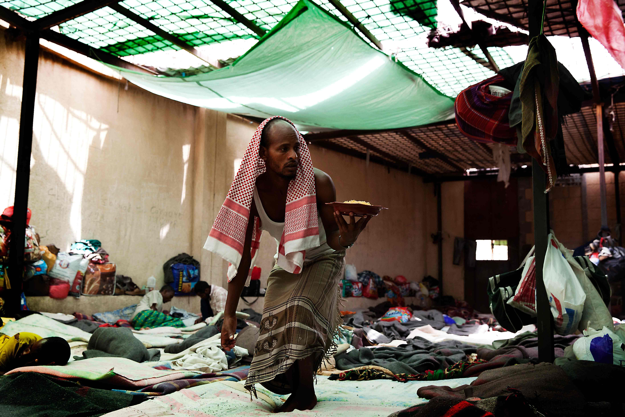 Un inmigrante, con su plato de comida camina por las zonas comunes del centro de detención/ Copyright: Anna Surinyach/MSF