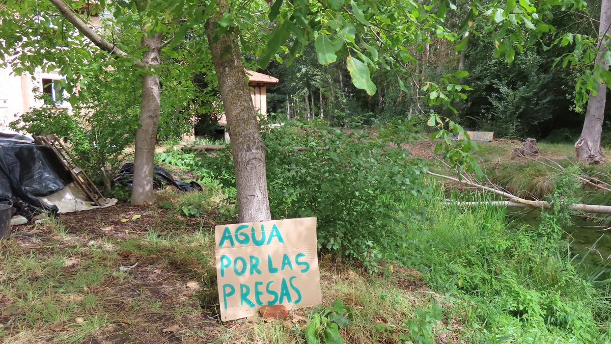 Un cartel que reclama el regreso del agua y, al fondo, el molino que Miguel Ángel Abella restaura.
