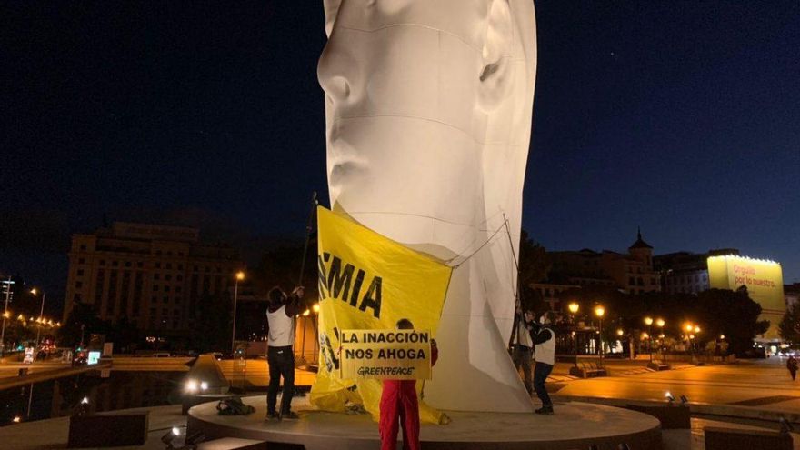 Activistas de Greenpeace colocan una pancarta a modo de mascarilla en la plaza de Colón de Madrid