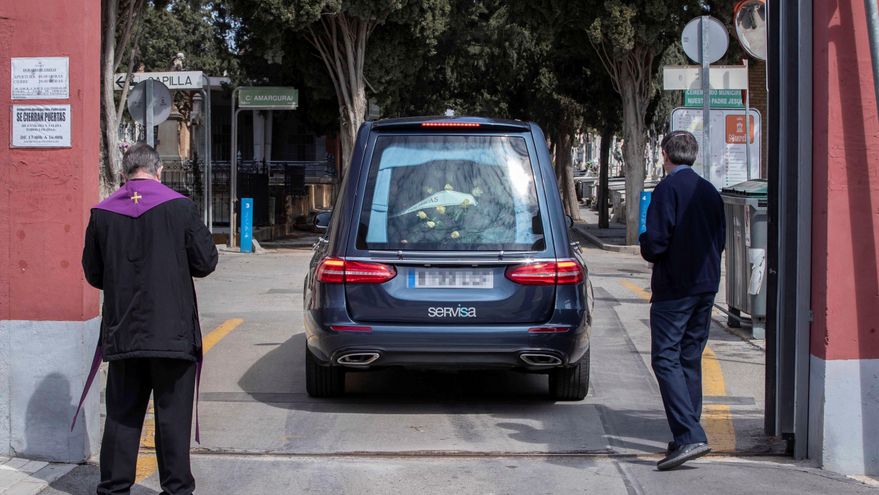 Un sacerdote y un familiar acompañan el coche fúnebre con los restos de un fallecido momentos antes del entierro. EFE/Marcial Guillén/Archivo