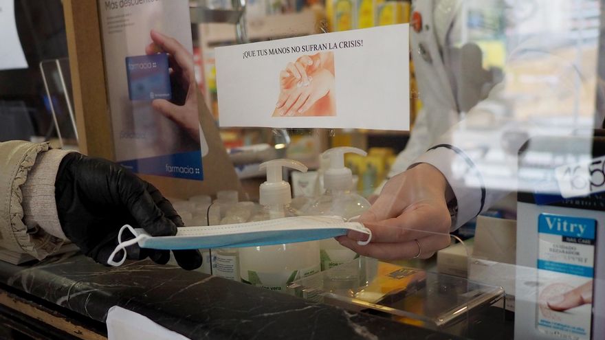 Archivo - Una persona coge una mascarilla que le da una trabajadora de una farmacia de Vitoria