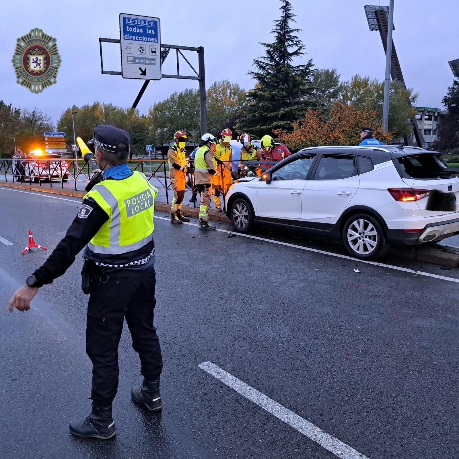 Numerosos bomberos intentando desincrustal el vehículo de la valla mientras la policía regula el tráfico.