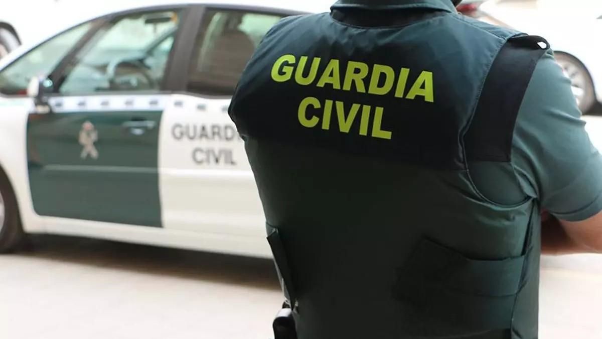 Imagen de archivo de un agente de la Guardia Civil, de espaldas, junto a un vehículo oficial.