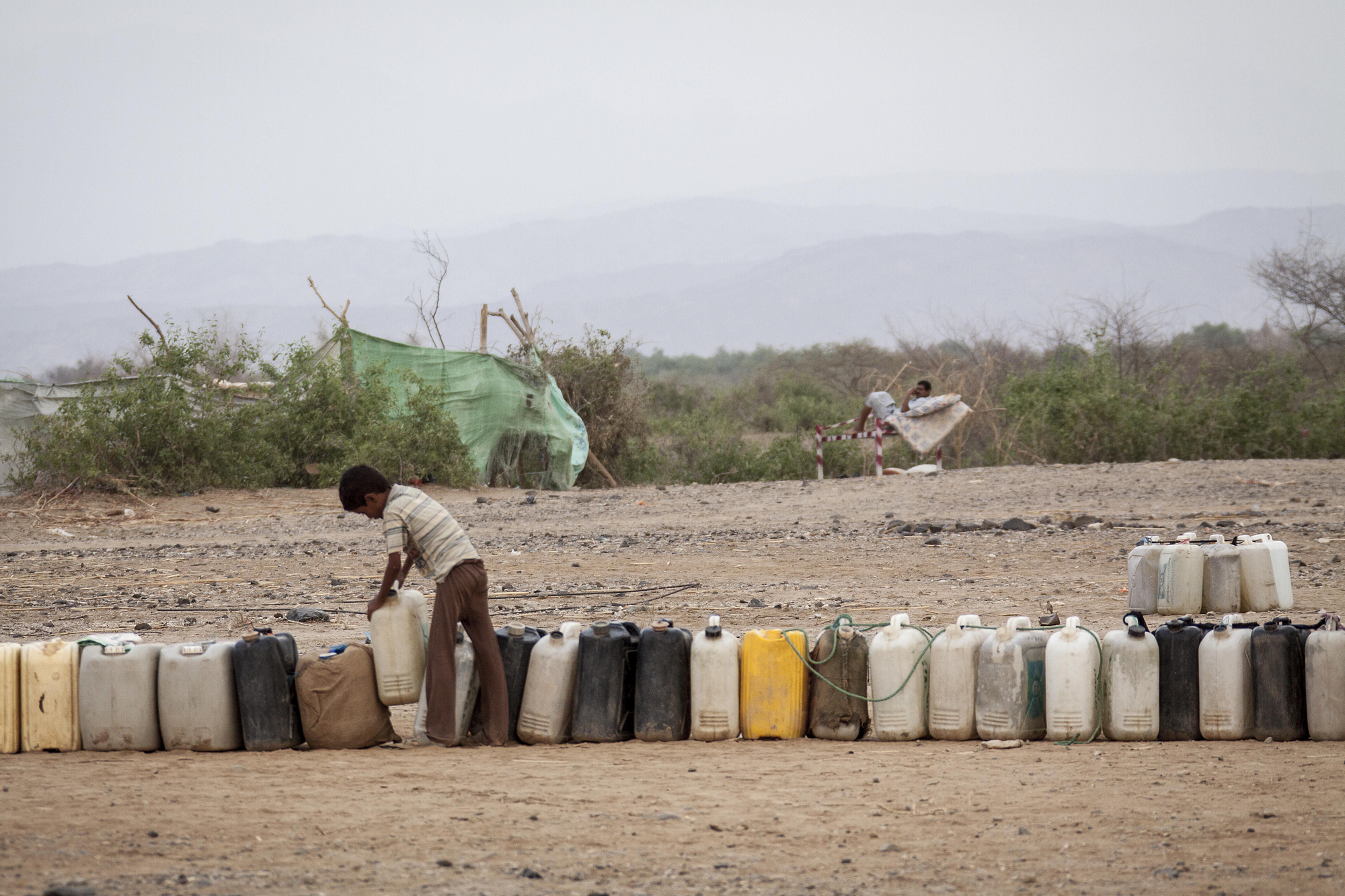 En Yemen, uno de los países con menos recursos hídricos del mundo y el agua debe ser bombeada con motores eléctricos. Sin embargo, la falta de combustible, está haciendo imposible extraerla y distribuirla y su precio se ha doblado en el último mes. Un niño desplazado en el asentamiento a las afueras de Beni Hassan, coloca en fila bidones vacíos mientras espera que comience la distribución de agua. Fotografía: Narciso Contreras/MSF