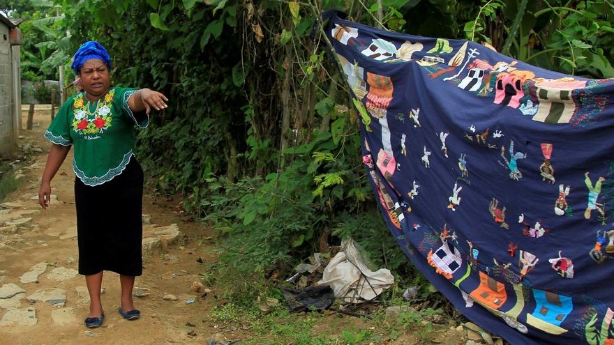 Fotografía del 15 de junio de 2020 que muestra a la defensora de derechos humanos y líder de la Asociación Mujeres Tejiendo Sueños y Sabores de Mampuján, Juana Ruiz, junto a un tapiz que cuenta la historia de la violencia vivida por los habitantes de Mampuján a manos de los paramilitares en el año 2000, en Mampuján (Colombia).