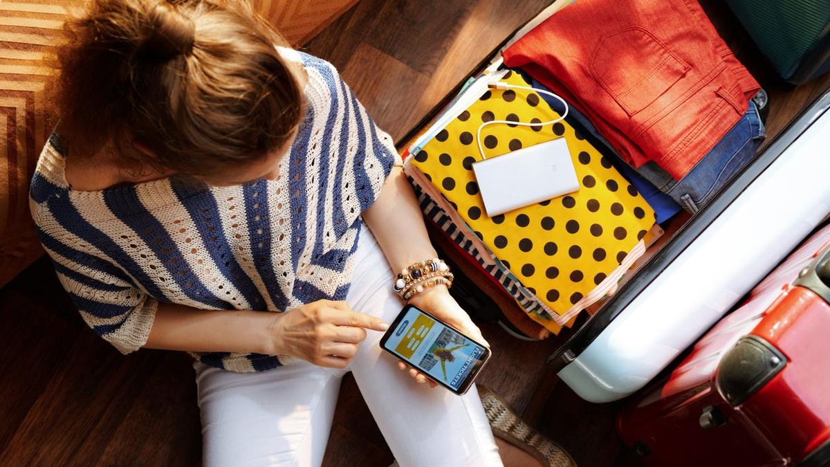Una mujer navega en Internet con su teléfono al deshacer su equipaje.