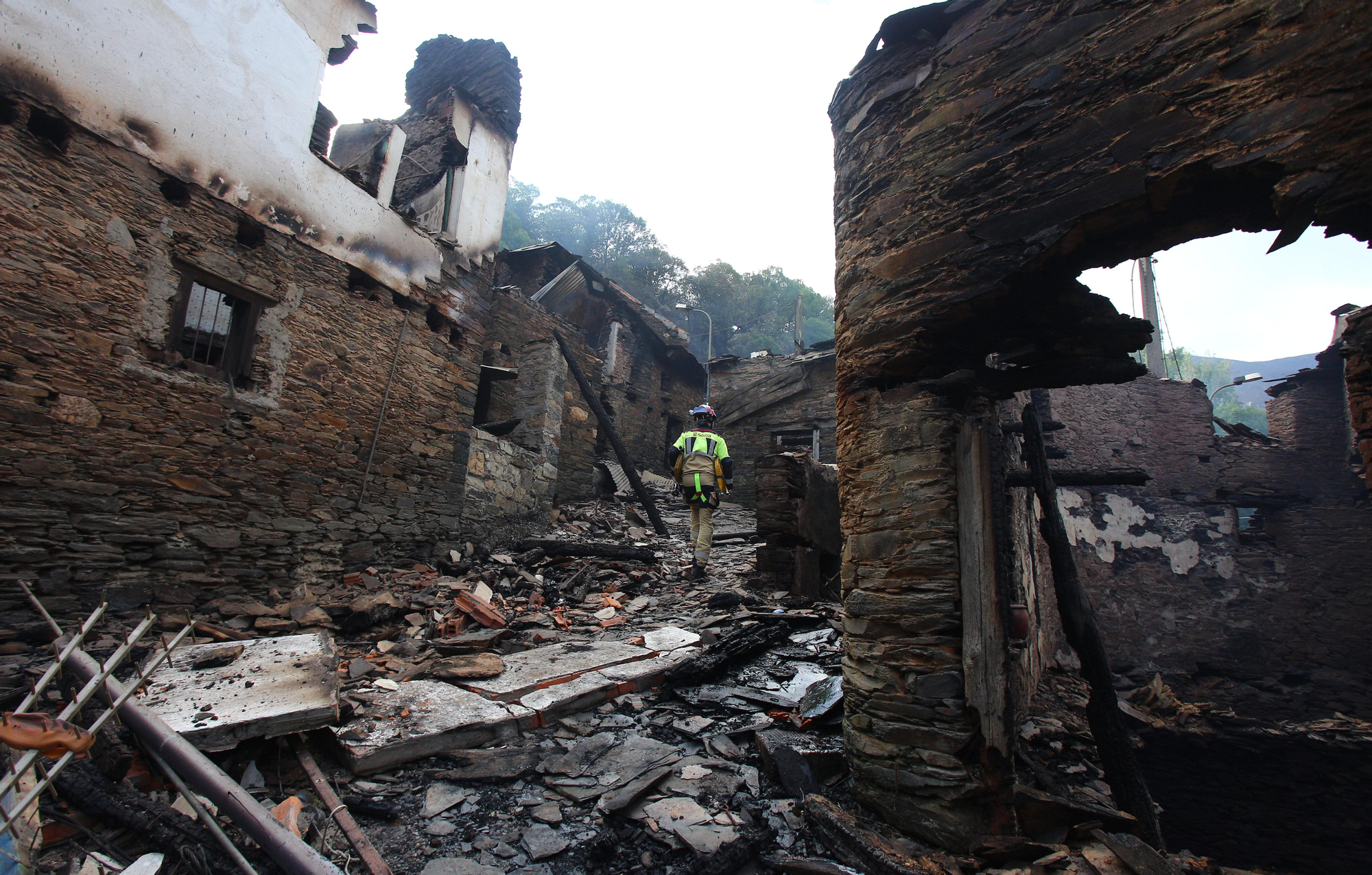Bomberos sorianos entre las casas destruidas por el fuego en el pueblo de Lusío, en El Bierzo.