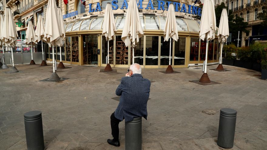Un hombre permanece sentado sobre un bolardo frente a bares y restaurantes cerrados en Marsella, Francia.