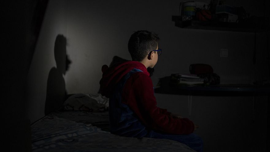 Mosaab, de 10 años, sentado en su habitación, iluminado por su padre con una linterna. / OLMO CALVO