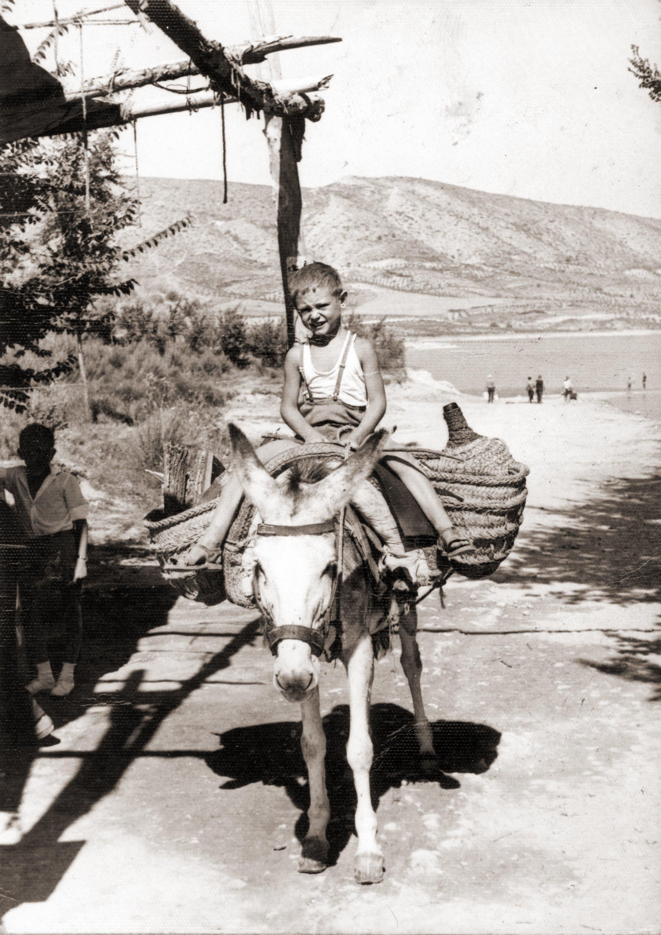 Niño subido en un burro transportando agua a uno de los merenderos que rodean el embalse de Buendía (Cuenca) durante el verano. 1960. Fondo Los Legados de la Tierra. Archivo de la Imagen de Castilla-La Mancha.