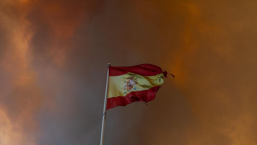 Una bandera de España con el humo de los incendios por detrás.