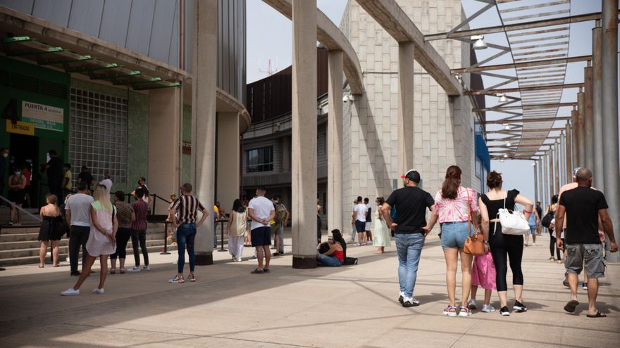 Varias personas esperan a ser vacunados (d) mientras jóvenes protestan (izq)