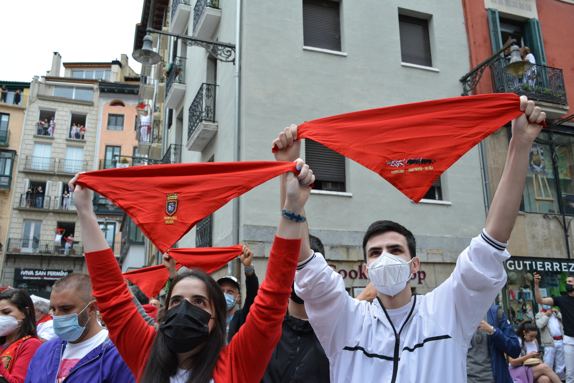 Varias personas levantan los pañuelos rojos a las 12 del mediodía en la plaza del Ayuntamiento de Pamplona