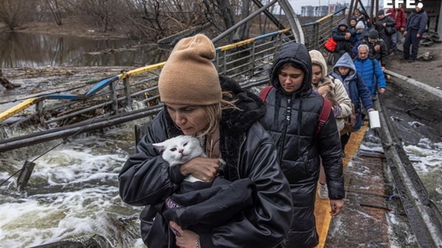 Una mujer con su gato cruza un puente destruido en la ciudad de Irpín, cerca de Kiev. EFE/ Roman Pilipey