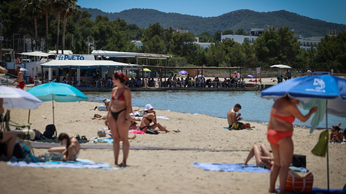 Turistas se bañan en la playa, al fondo, el chiringuito.