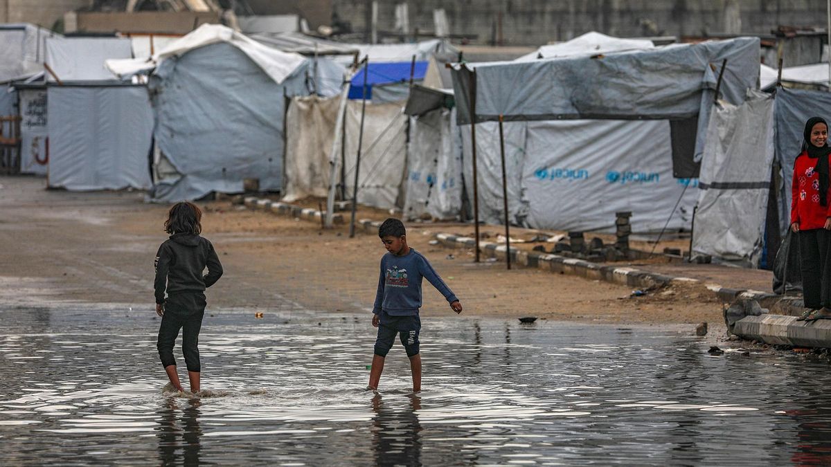 Um grupo de crianças palestinianas deslocadas brinca numa poça fora do campo temporário onde vivem.