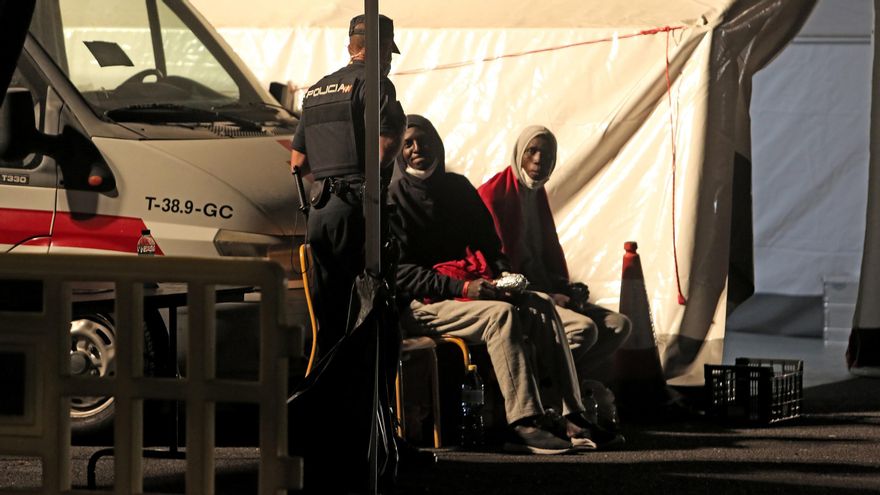 Dos migrantes hablan con un agente de la Policía Nacional en el campamento de Arguineguín