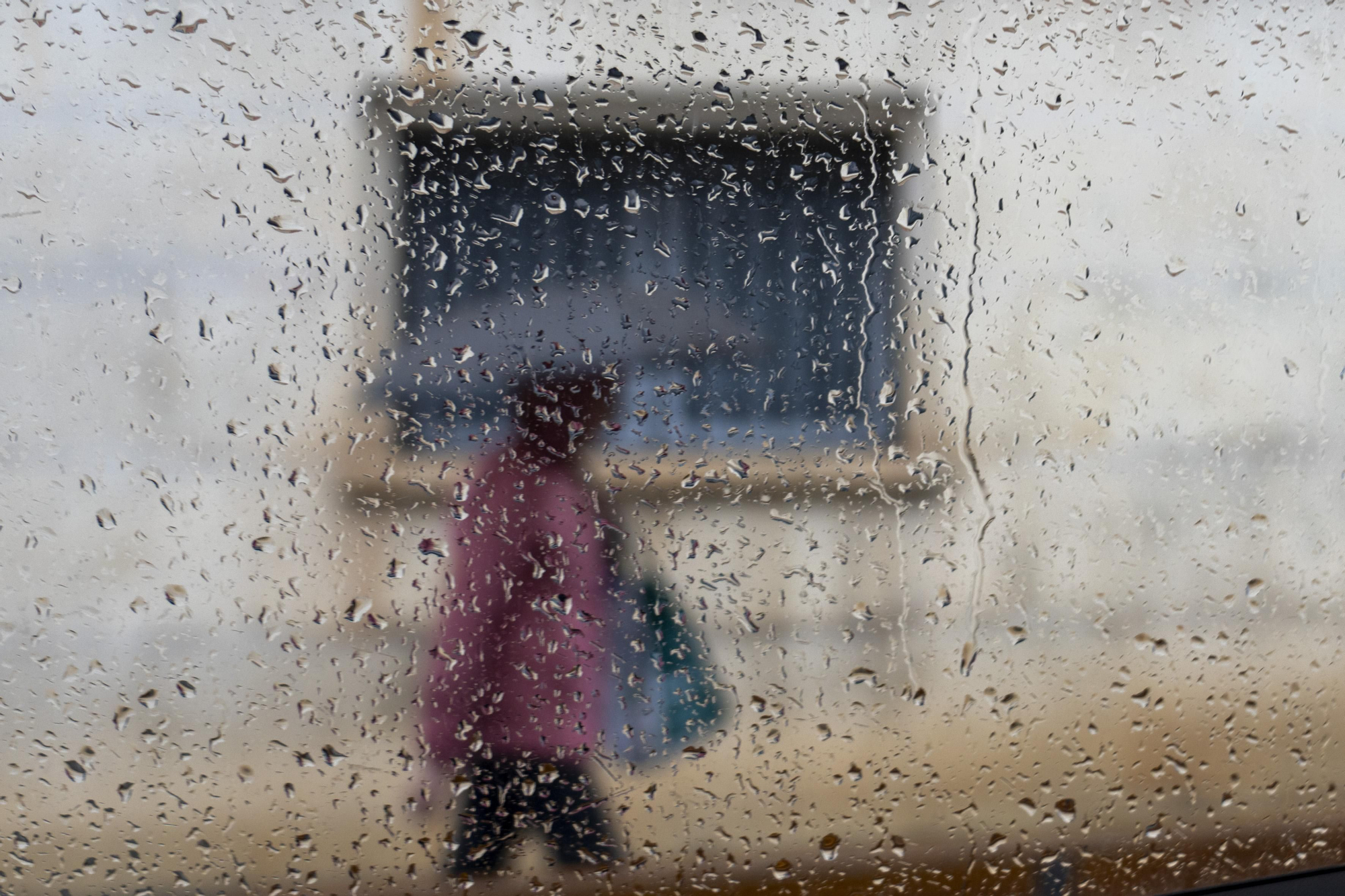 Una persona vista a través de un cristal mojado camina bajo la lluvia en una imagen de archivo. EFE/Antonio Garcia