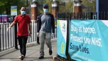 Dos personas caminan con mascarilla junto a un cartel de la NHS, en Reino Unido
