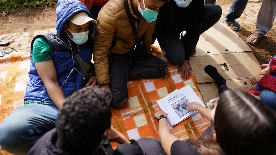 Una voluntaria enseña algunas frases en español a un grupo de inmigrantes en el exterior del campamento