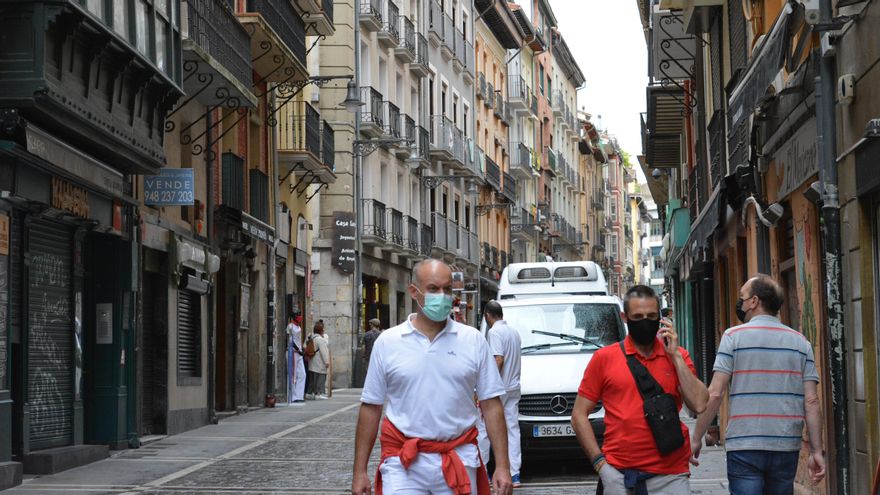 Dos personas caminan por la calle Estafeta de Pamplona vestidos de blanco y rojo