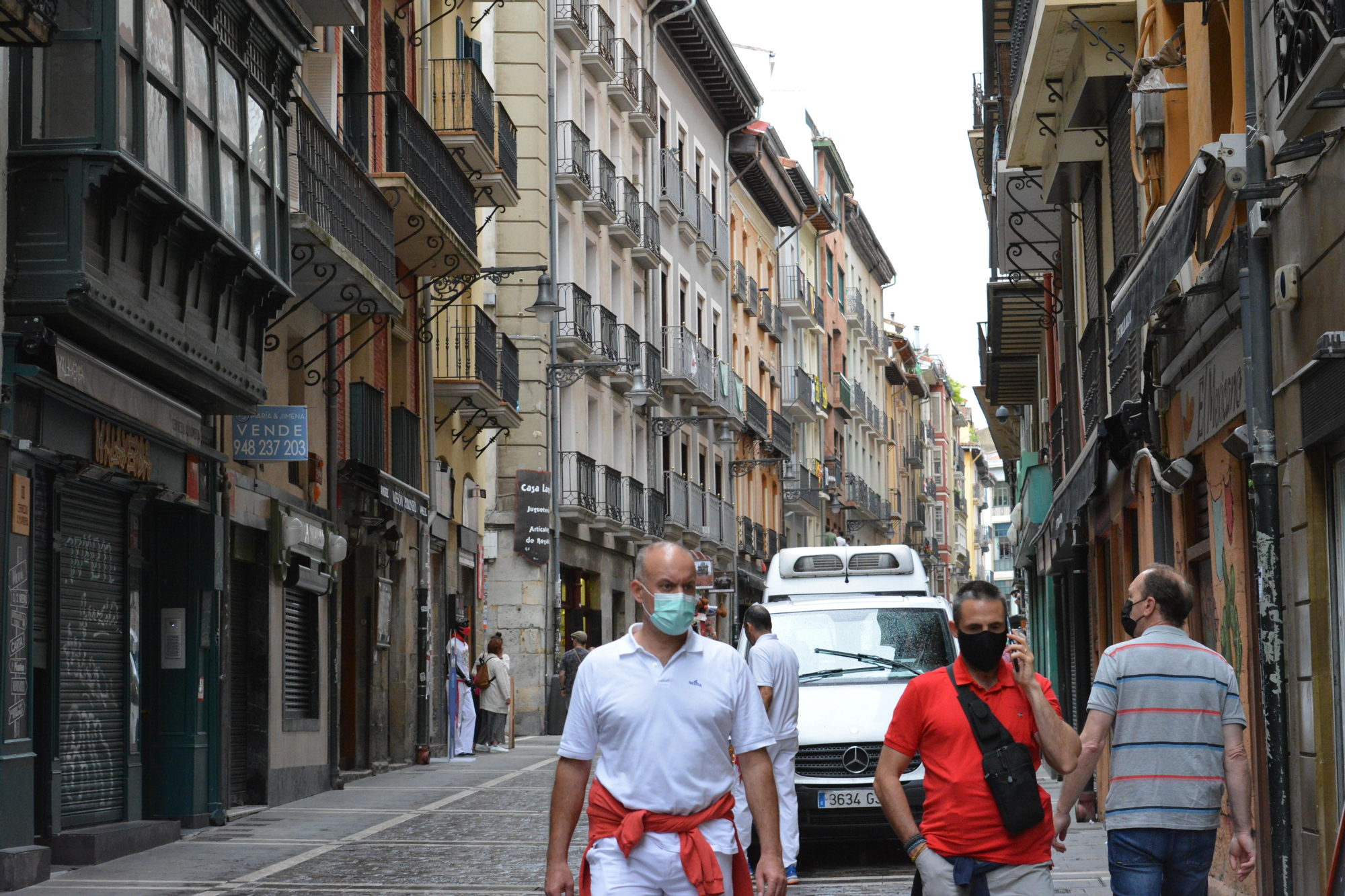 Dos personas caminan por la calle Estafeta de Pamplona vestidos de blanco y rojo