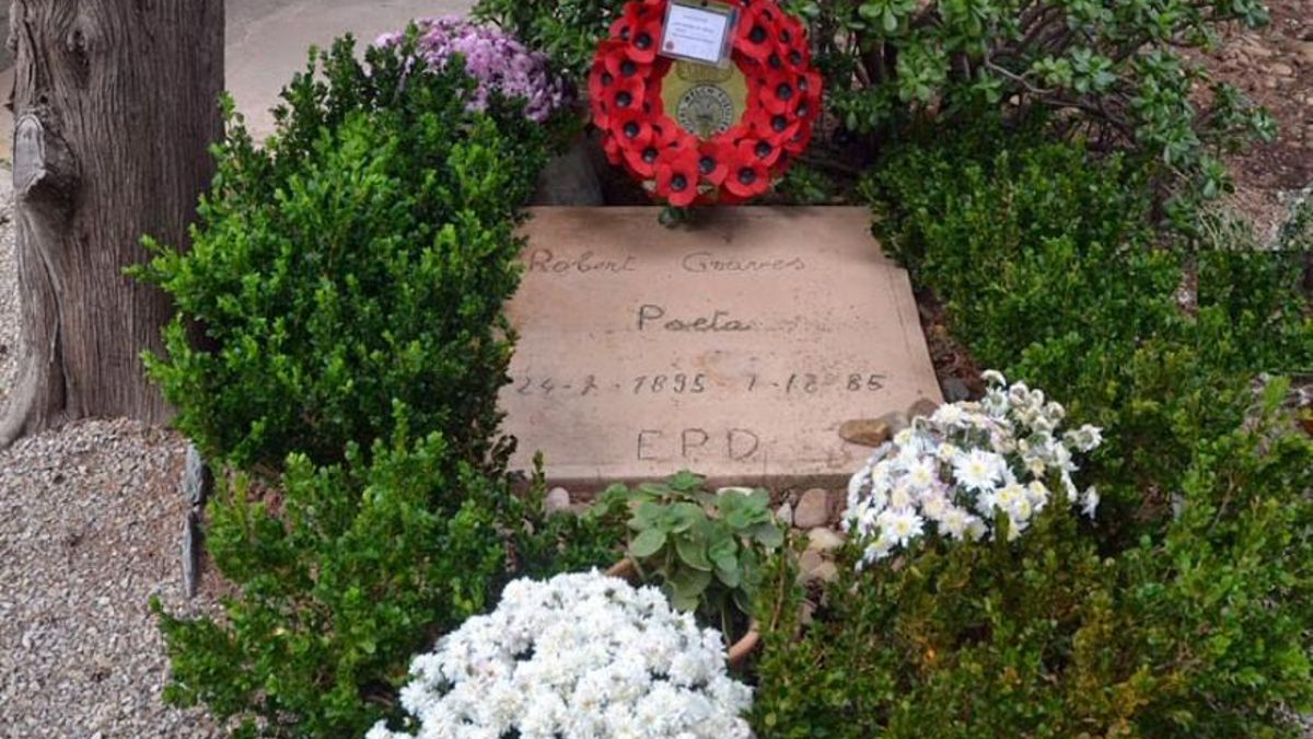 Tumba de Robert Graves en el cementerio de Deià, bajo un ciprés y rodeada de flores, con la sencilla inscripción “Poeta”.