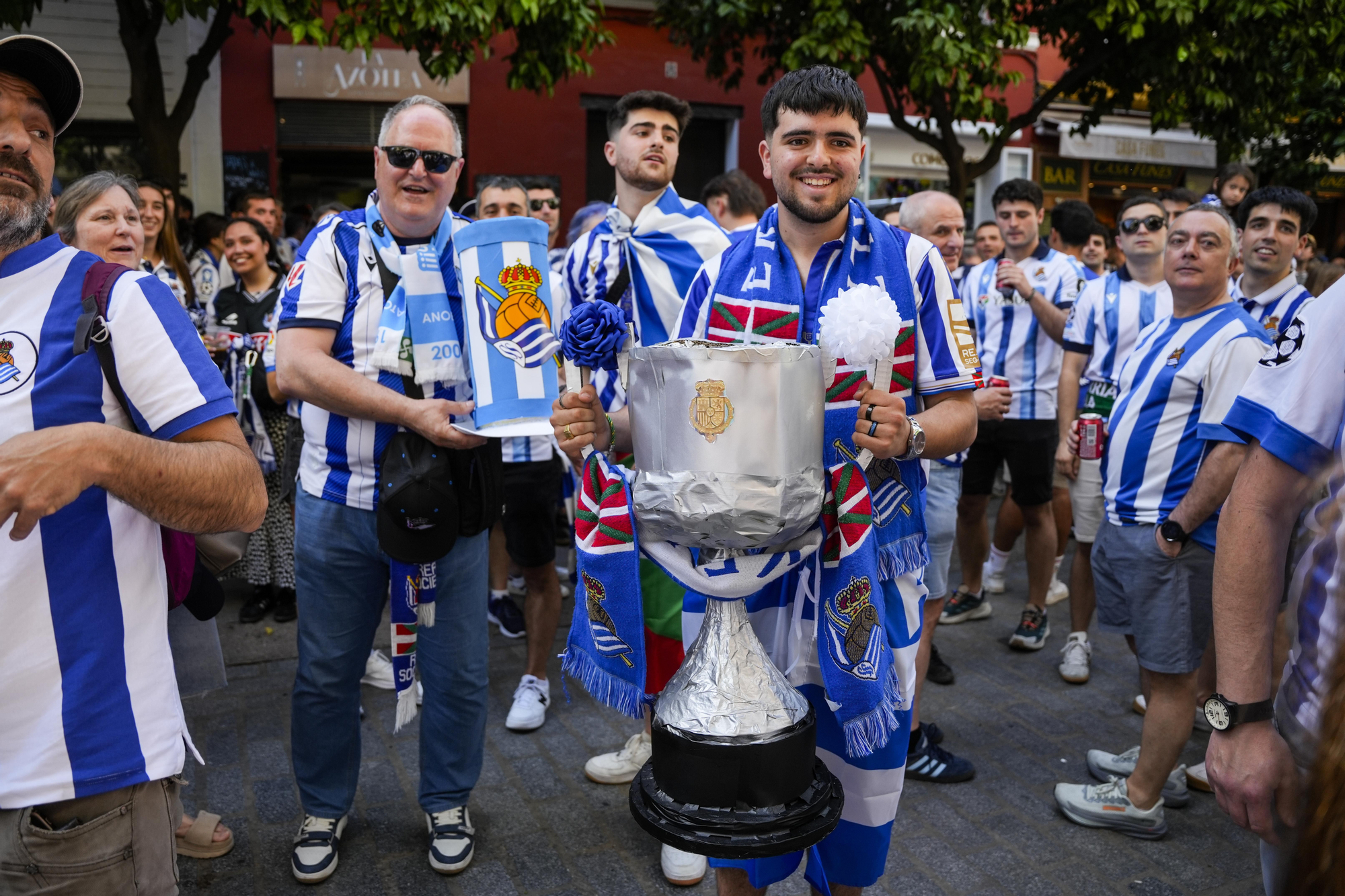 Aficionados de la Real Sociedad posan con una réplica de la Copa del Rey en Sevilla.