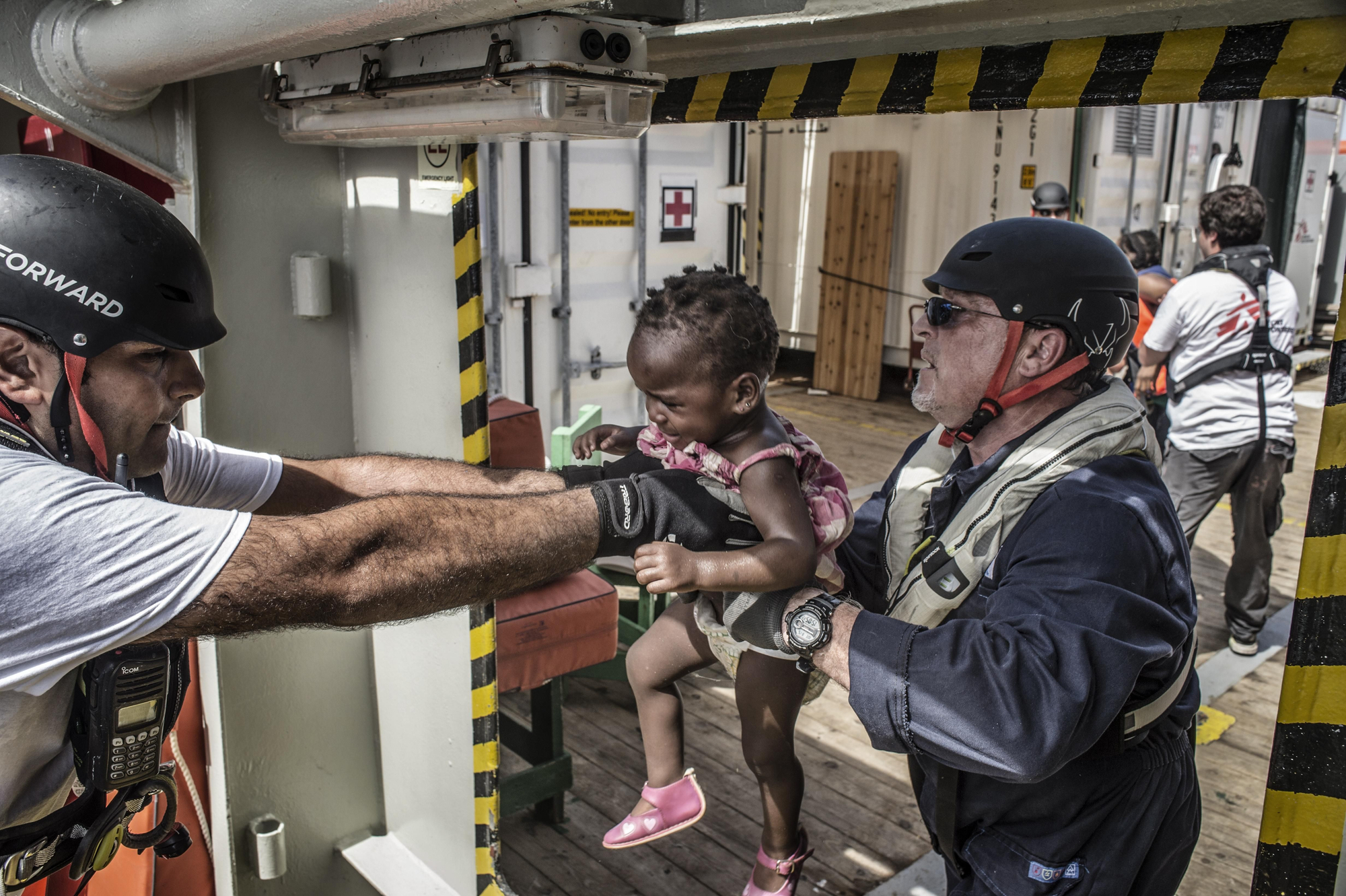 Nael Nasser (de azul), mediador cultural a bordo del Bourbon Argos ayuda a una niña tras quitarle su pequeño salvavidas. “En su desesperación, los padres y madres arrojan a sus hijos a nuestros brazos y confían ciegamente en unos extraños como nosotros para que los llevemos al barco de rescate. Resulta desgarrador ver cómo familias con niños de tan solo unos meses de edad en este tipo de situaciones límite" afirma Sebastian Stein, coordinador de MSF en el Argos. Fotografía: Francesco Zizola/NOOR