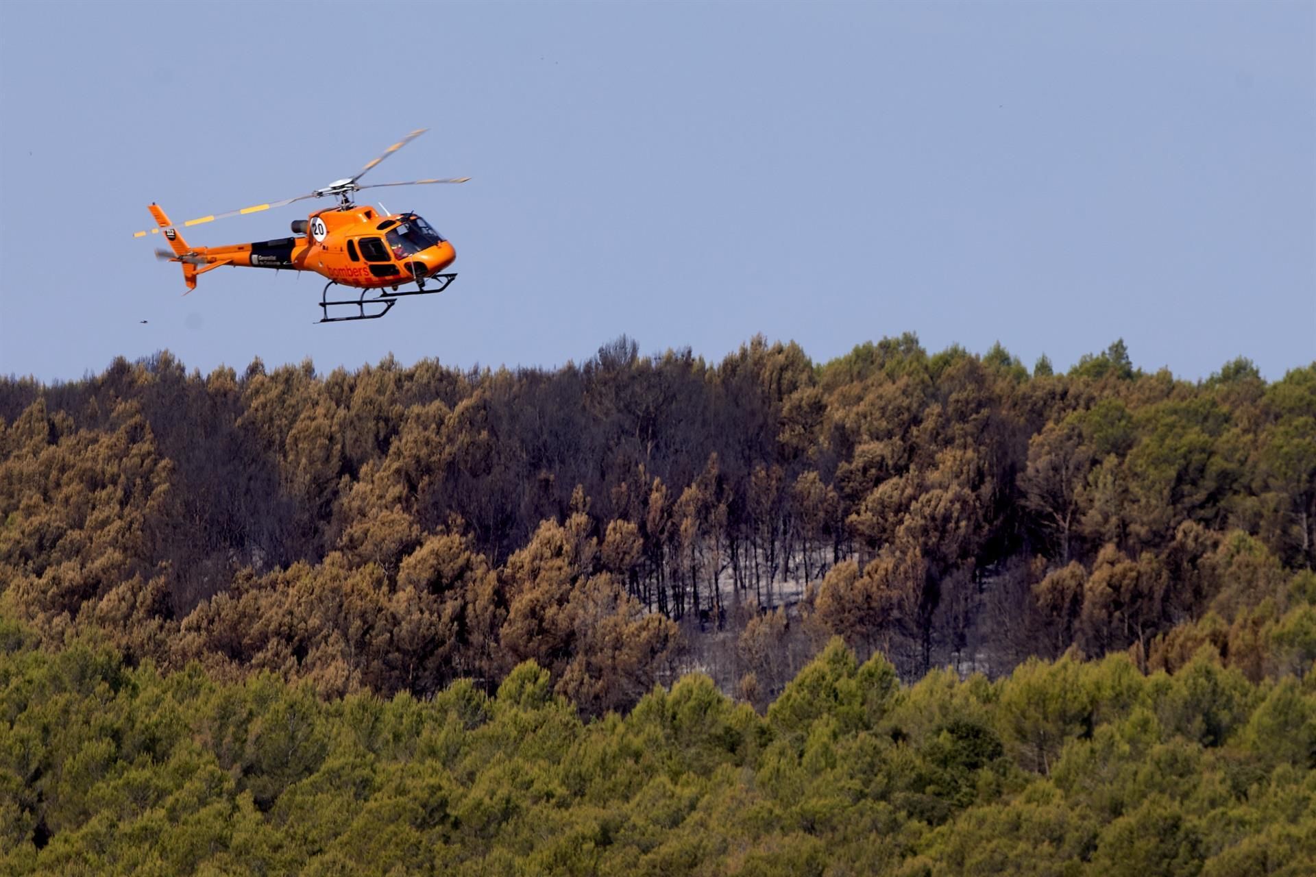 Un helicóptero sobrevuela este domingo un paraje forestal en la zona afectada por el incendio declarado en Ventalló (Girona)