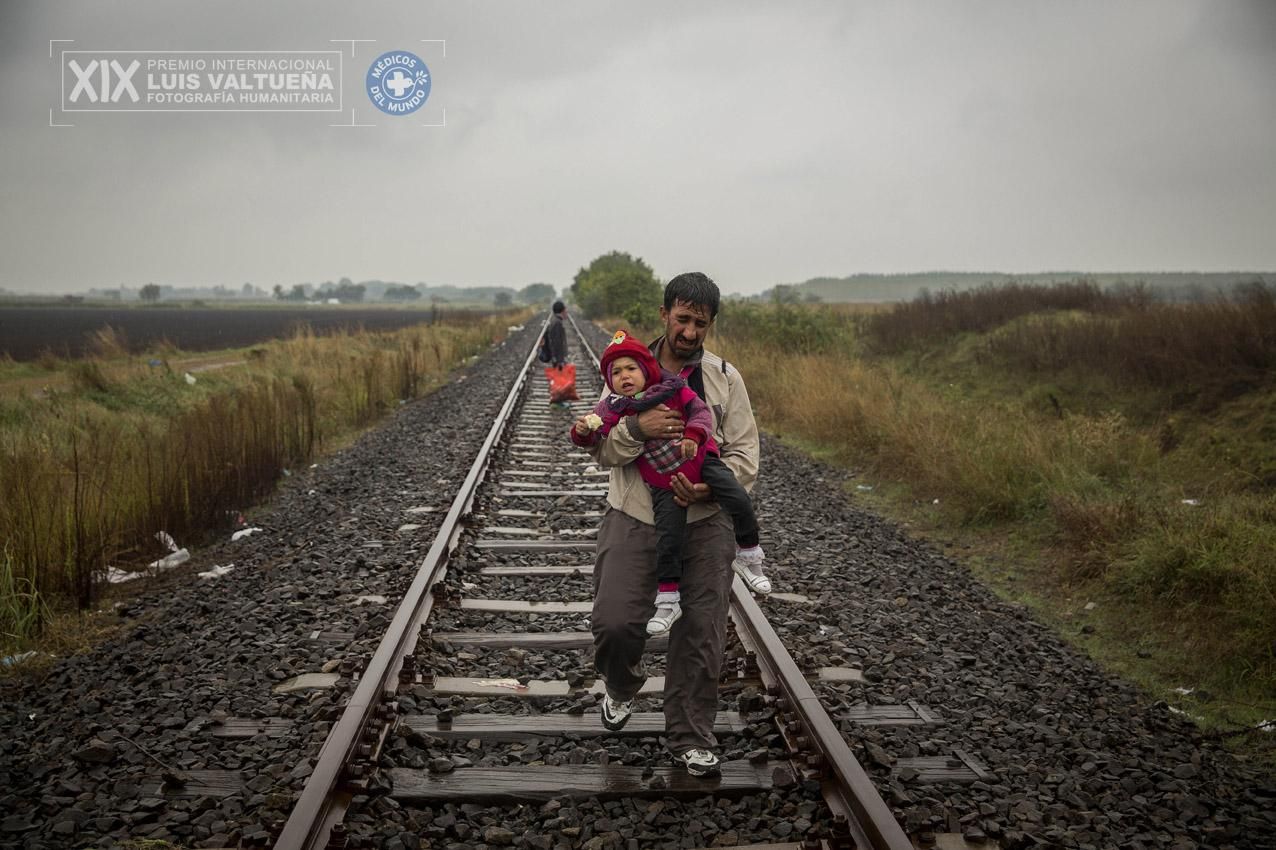 Un padre camina por las vías del tren con su hijo pequeño en brazos tras haber cruzado la frontera entre Serbia y Hungría, entrando en la localidad de Roszke. (Hungría. 10/09/2015). | Foto: Olmo Calvo.