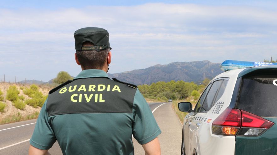 Archivo - Un agente de la Guardia Civil junto a un vehículo en una carretera.