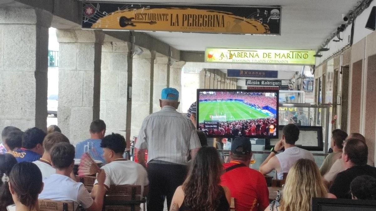 Varios turistas, algunos de ellos peregrinos, ven el España-Arabia Saudí del pasado 21 de junio en la terraza de un bar en Portomarín (Lugo) mientras un paisano la atraviesa.