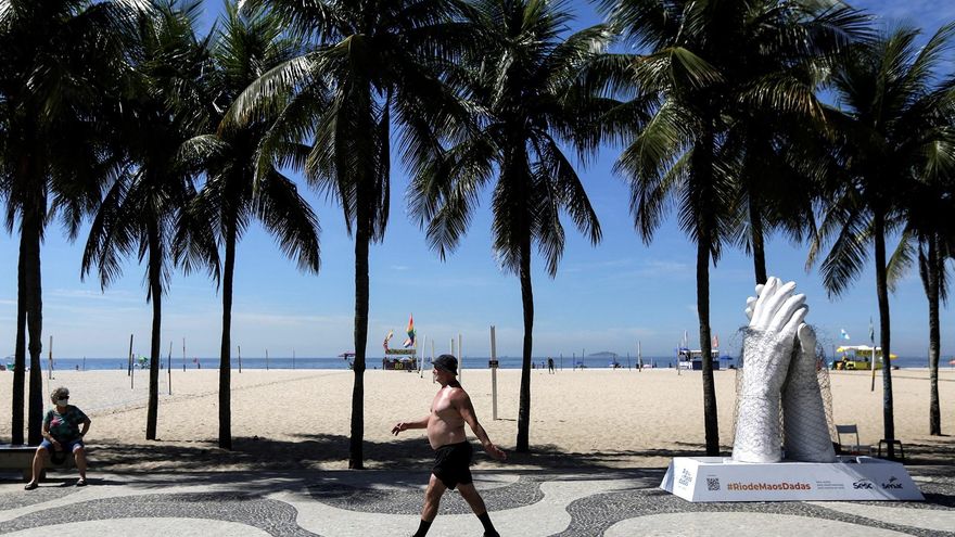 Un hombre camina cerca a una escultura de manos estrechadas hoy, en la playa de Copacabana, en Río de Janeiro (Brasil). EFE/Antonio Lacerda