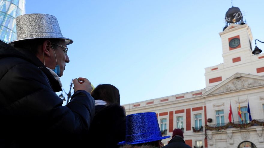 Unas personas se comen las uvas aprovechando las campanadas de las doce del mediodía en la Puerta del Sol este jueves, último día del año que nos dejará unas campanadas insólitas ya que la Puerta del Sol estará vacía debido a las restricciones por el coronavirus. EFE/Fernando Alvarado