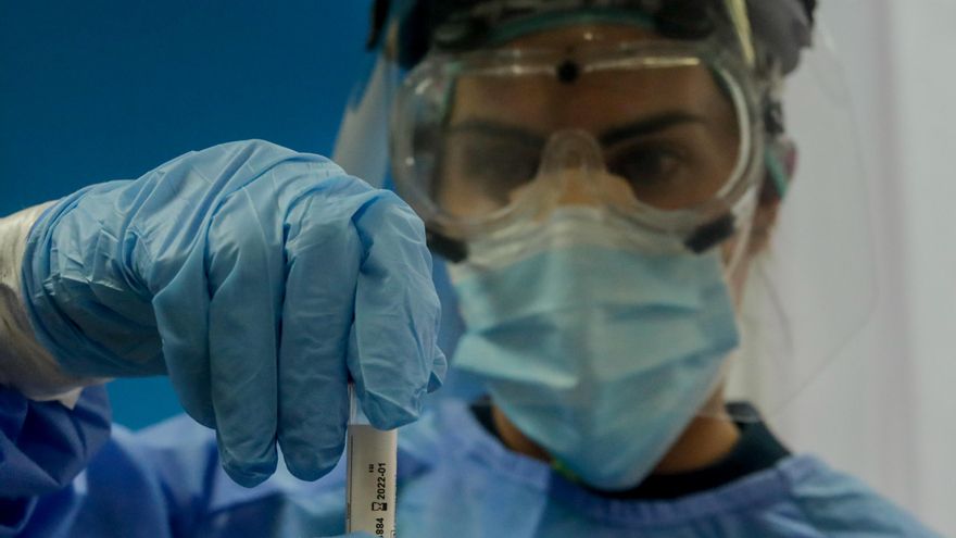 Una trabajadora sanitaria sostiene una probeta con una prueba PCR.