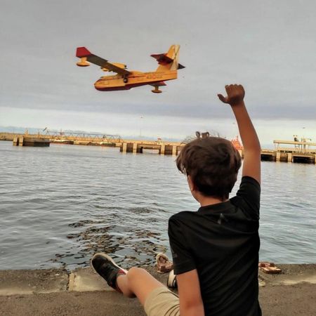 Un niño saluda a un hidroavión mientras realiza una carga de agua en el puerto de Santa Cruz de Tenerife este agosto