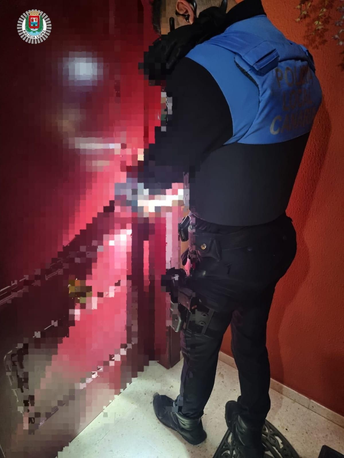 Un agente de la Policía Local de Las Palmas de Gran Canaria en la puerta del domicilio de la mujer que tuvo que ser auxiliada tras pasar varios días en el suelo.