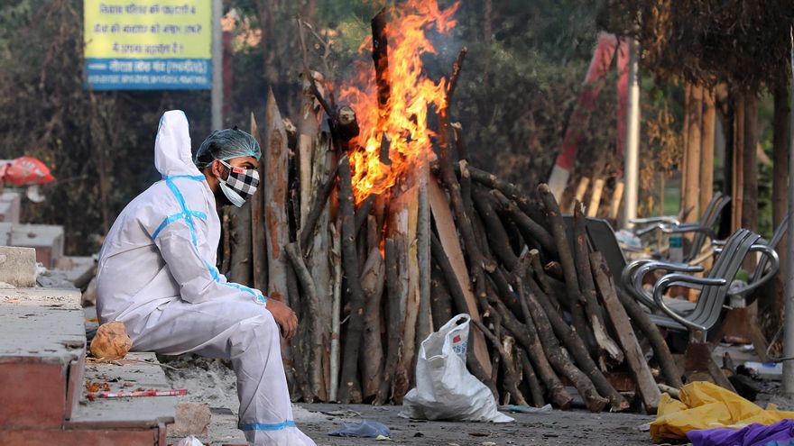 Un hombre ataviado con un traje aislante descansa tras realizar rituales funerarios a sus familiares difuntos en Nueva Delhi. EFE/ Harish Tyagi