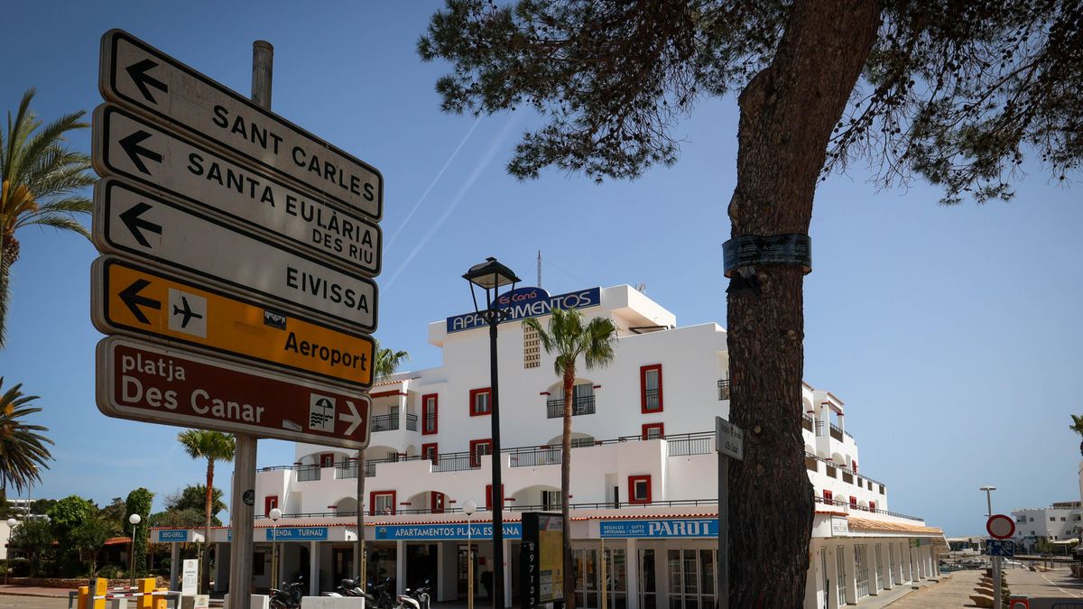 Una señal con indicaciones y al fondo un bloque de apartamentos turísticos.